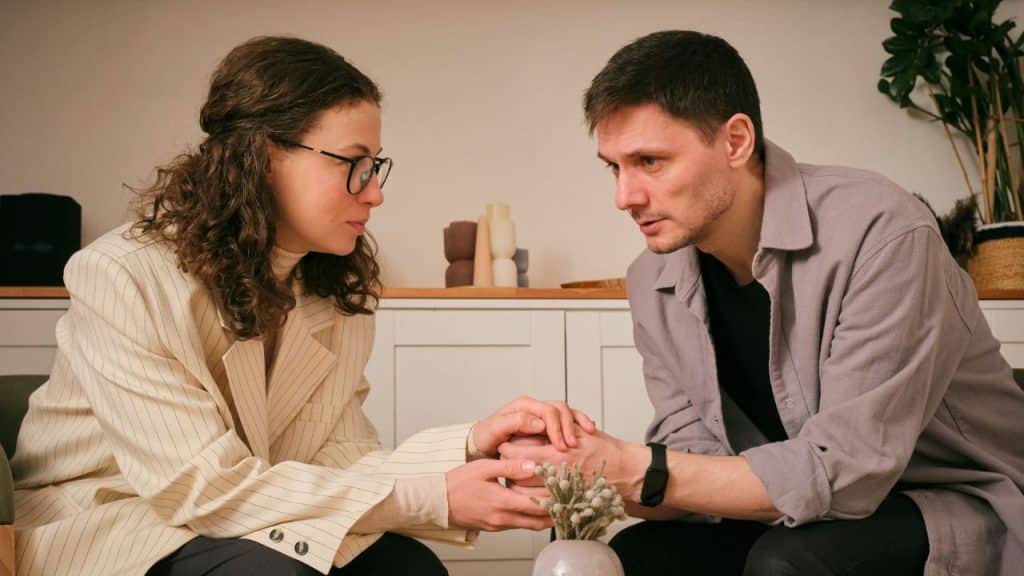 A man and woman sit facing each other and hold hands over a small table.