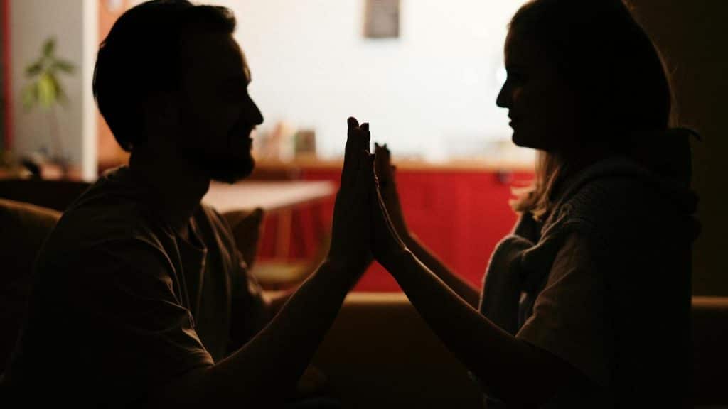 A couple sits facing each other with their hands pressed together.