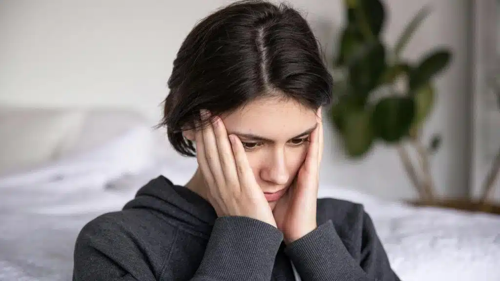 A worried woman sitting indoors holding her head in her hands.