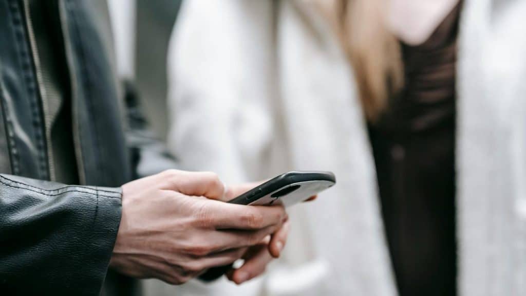 A person holding a smartphone while standing next to someone.