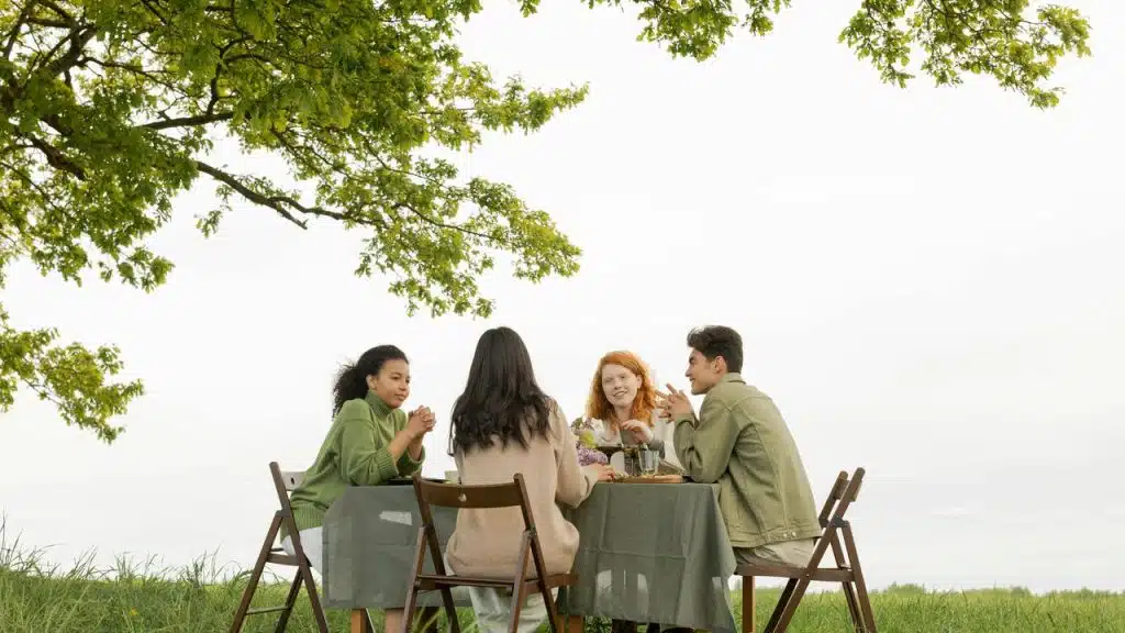 A group of friends sitting at a table outdoors under a tree.