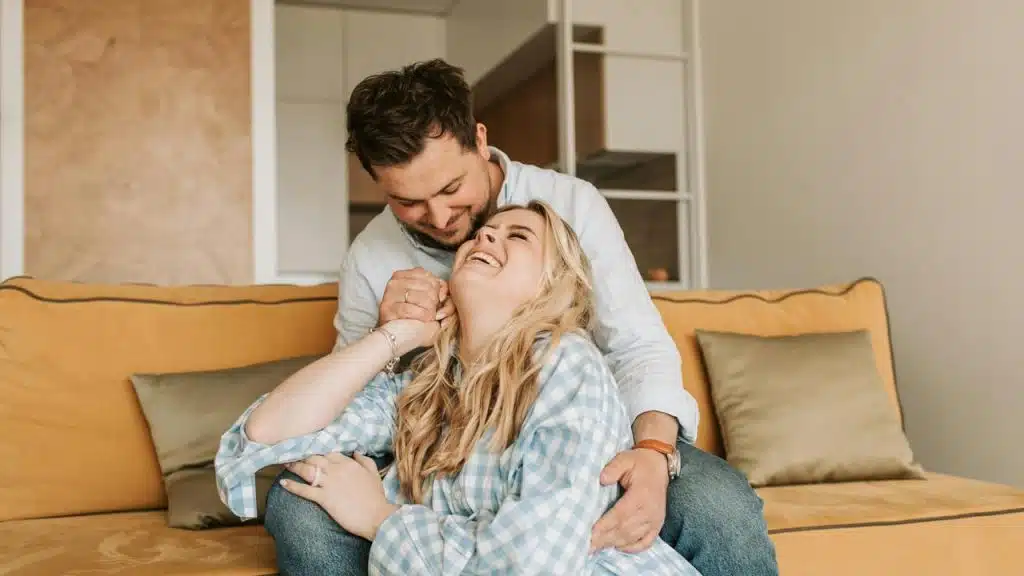 A couple laughing together while sitting on a couch.