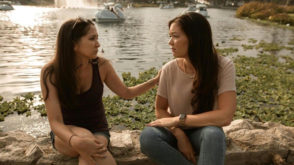 An upset woman comforting a friend during a serious conversation by a lake.