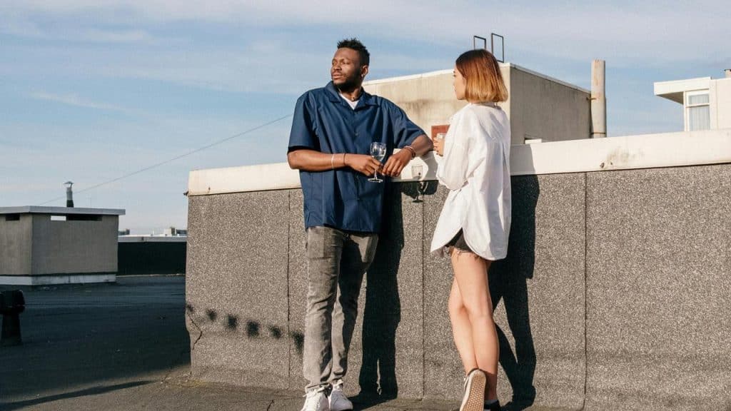 A man and a woman talking on a rooftop while holding drinks.