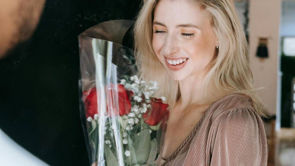 A smiling woman holding a bouquet of red roses.