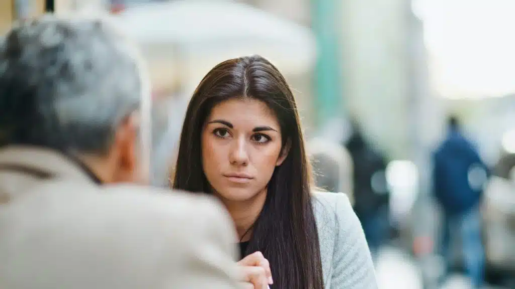 A woman with a serious expression looks toward a person partially out of frame.