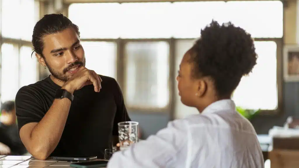 A man rests his chin on his hand while talking to a woman.