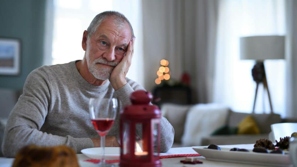 An older man sits at a table with his head resting on his hand.