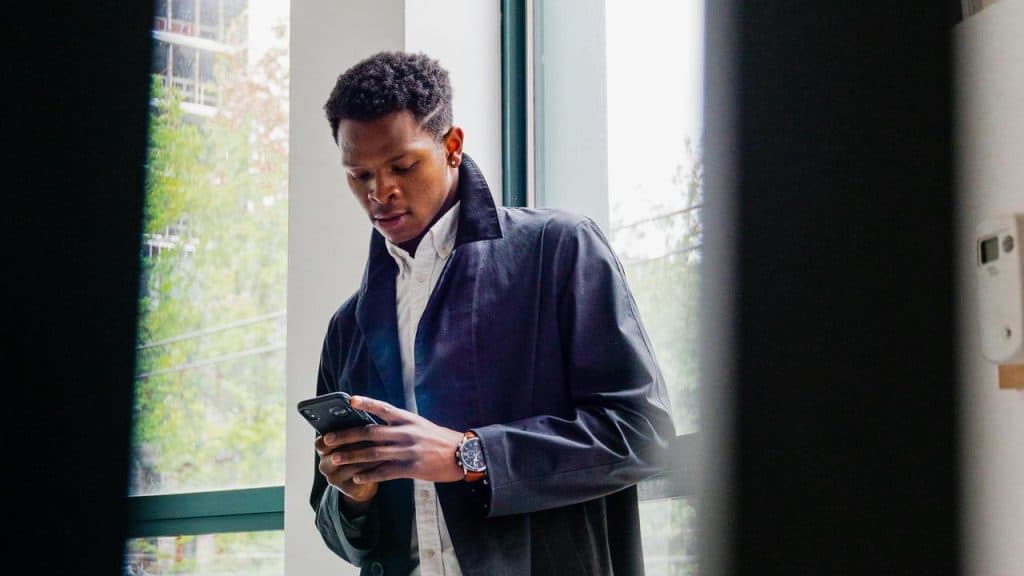 A man standing by a window and looking at his phone.