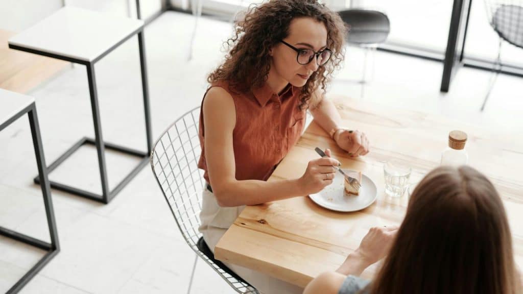 A woman talking while eating dessert at a table with another person.