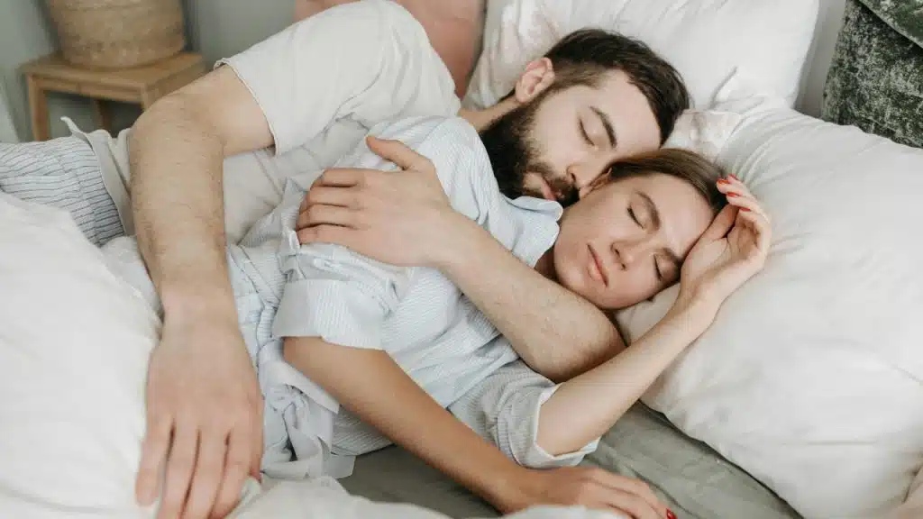 A man and woman sleeping peacefully in bed while holding onto each other.