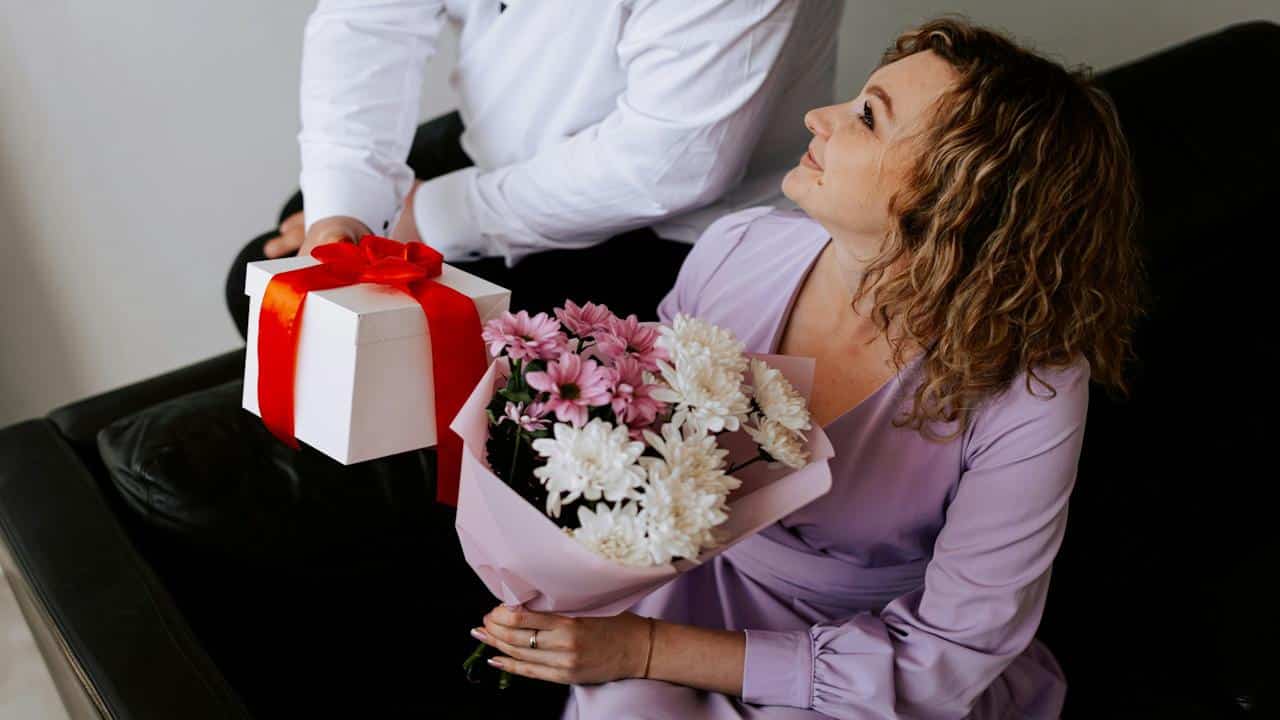 A man giving a present and a bouquet of flowers to his wife.