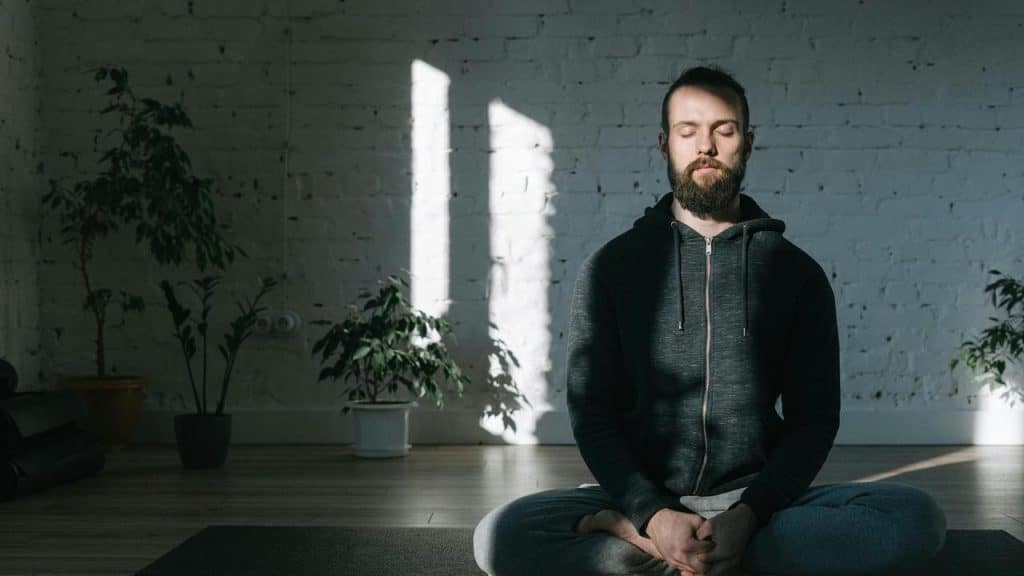 A man meditating on a yoga mat in a bright room.