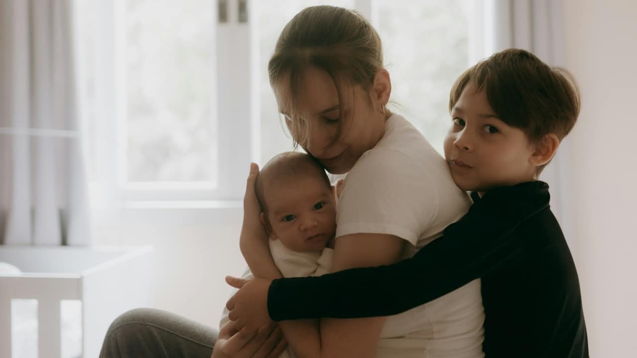 Woman holding a baby while a boy embraces them in a bright indoor setting