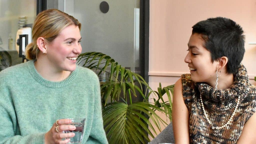A woman smiling while talking with a friend indoors.