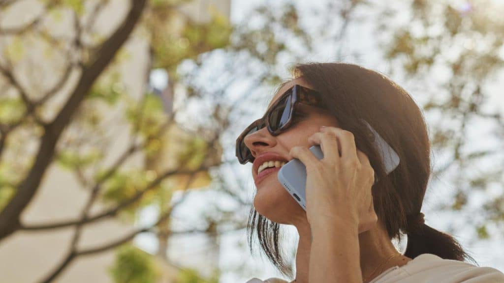 A woman wearing sunglasses and talking on her phone outdoors.
