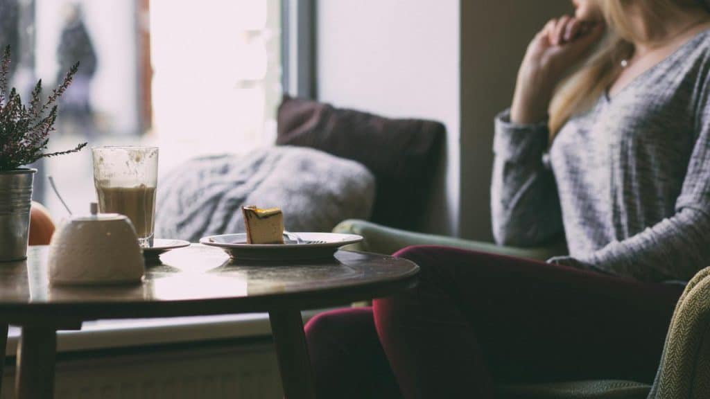A woman sitting by a table with coffee and cake.