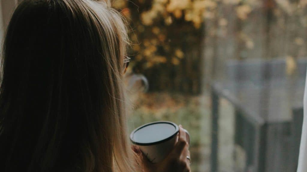 A person holding a cup while looking out a window.