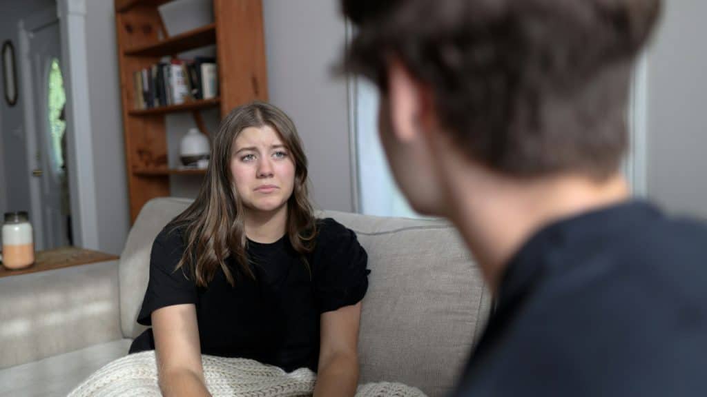 A tearful young woman looks at an out-of-focus person sitting before her.