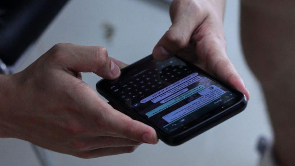 A close-up shot showing two hands holding a smartphone while typing a message on a keyboard.