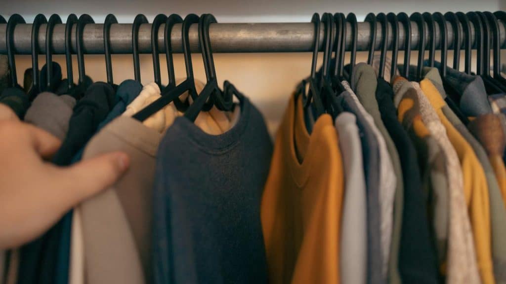 A hand browsing through neatly hung shirts on a clothing rack.