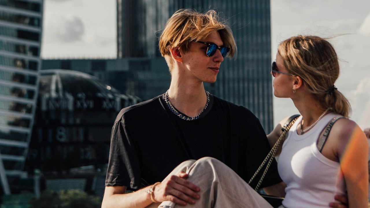 A man and a woman sitting on a ledge in front of a cityscape.