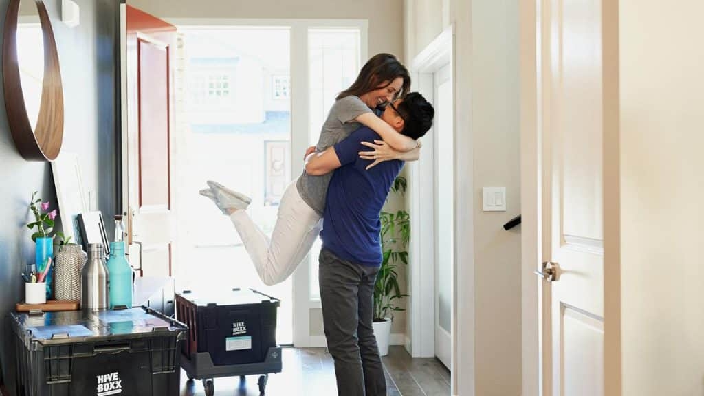 A couple hugging joyfully in a doorway surrounded by moving boxes.