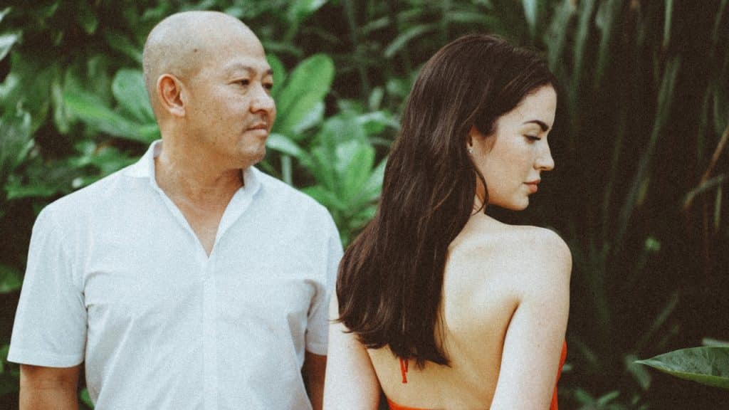 A man in a white shirt and a woman in orange stand against green foliage.