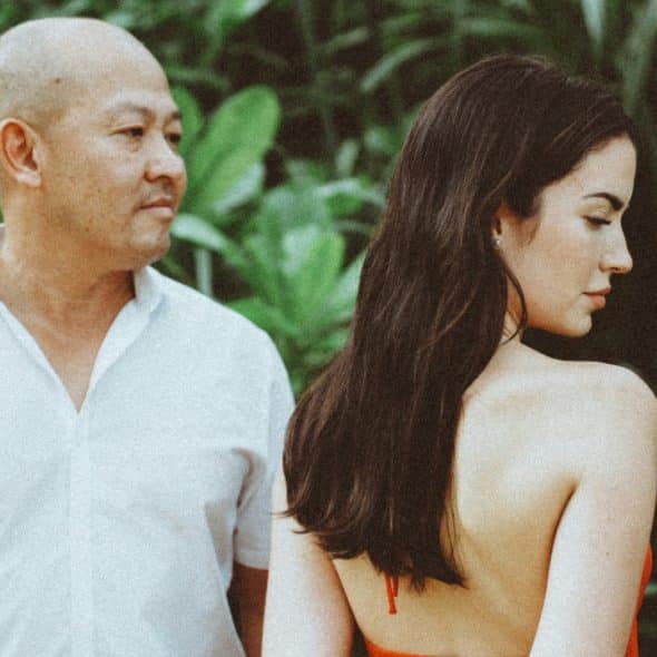 A man in a white shirt and a woman in orange stand against green foliage.