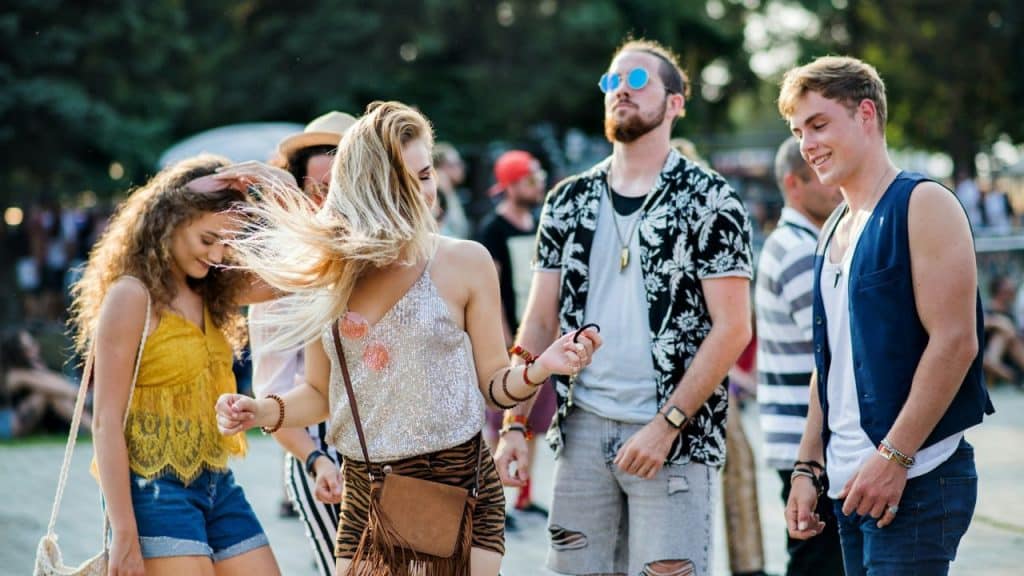 A group of young adults dance together outdoors at a sunny festival or public event.