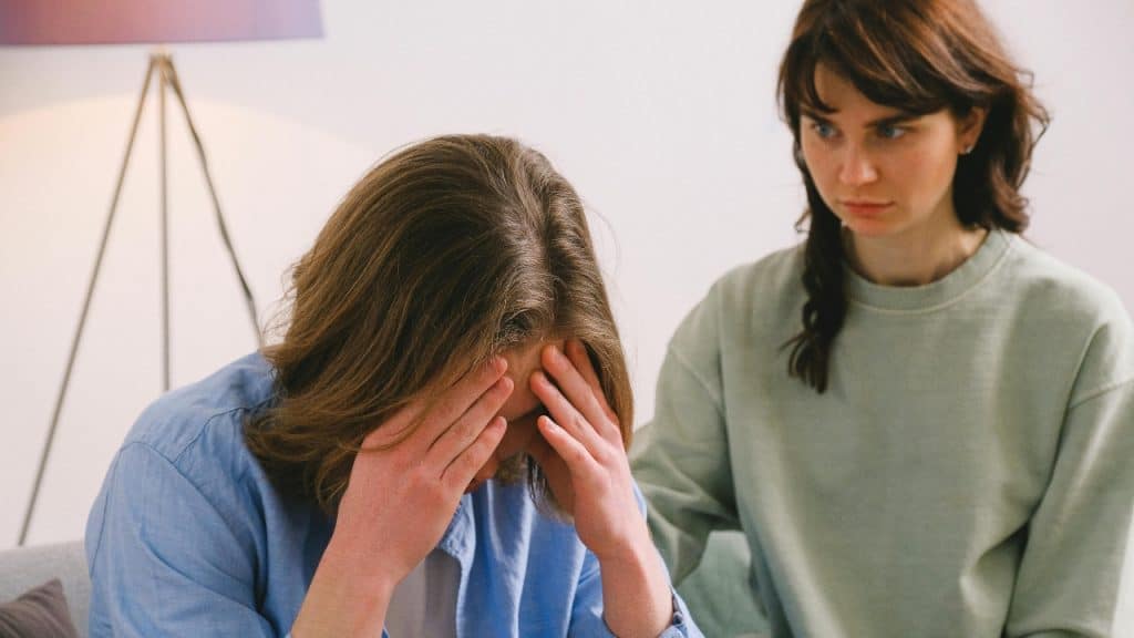 A man holds his head in his hands while a woman looks at him sternly.