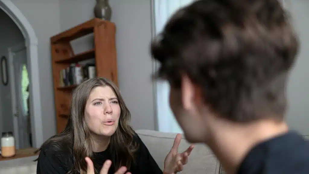 A woman complaining to her husband while sitting on a couch with him.