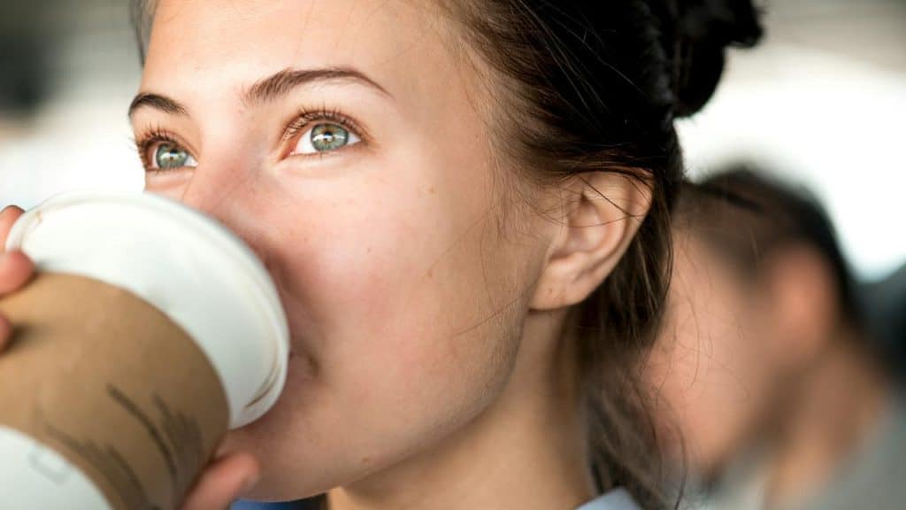 A woman drinking from a takeaway coffee cup.