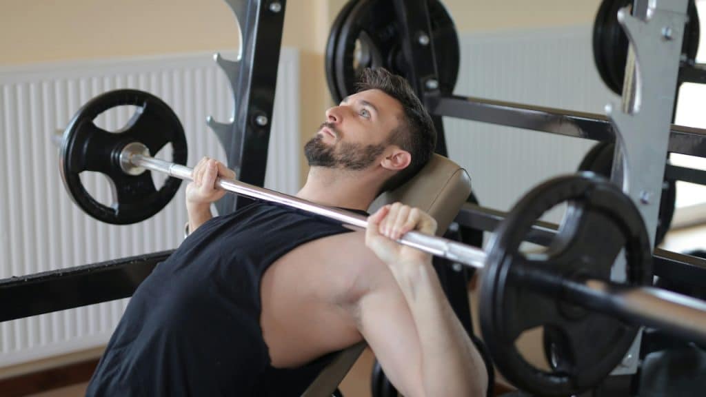A man lies on an inclined weight bench while gripping a barbell in a gym.