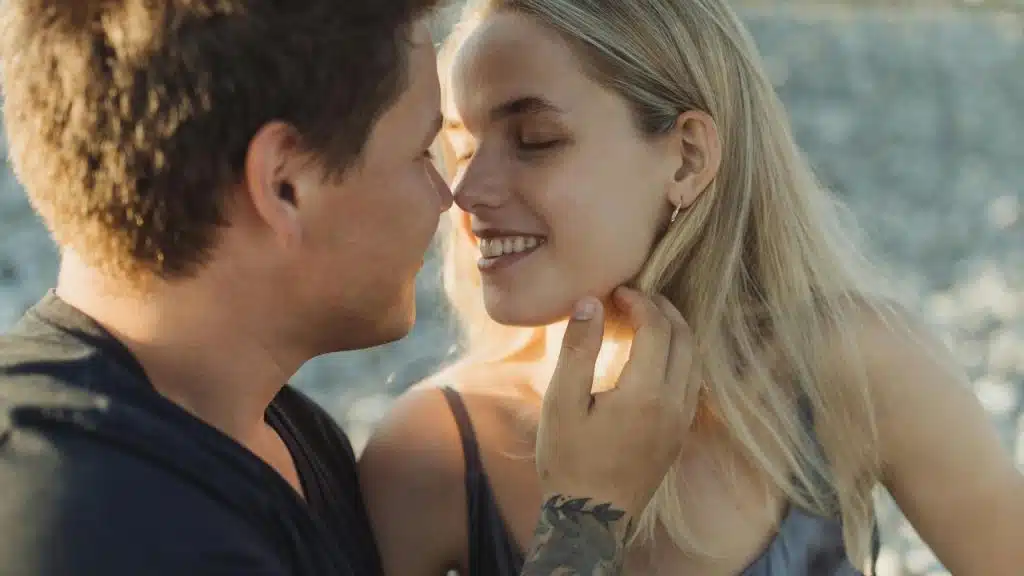 A close-up of a couple smiling and leaning in for a kiss outdoors in warm sunlight.