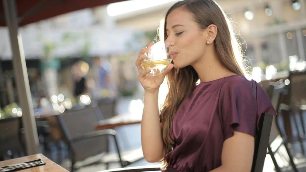 A woman sitting outdoors drinking from a glass of white wine.