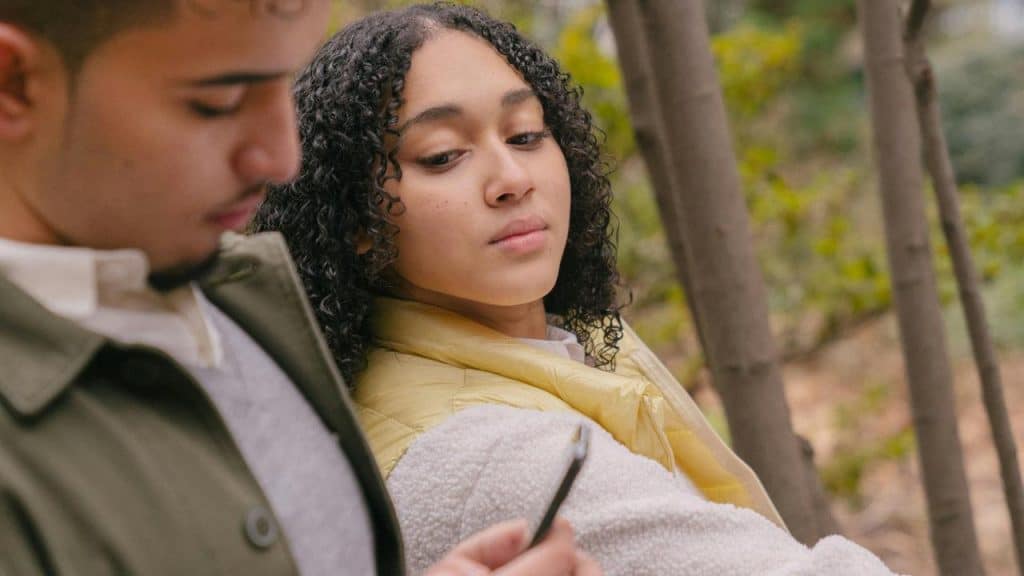 A woman looking at a man’s phone while standing outdoors.
