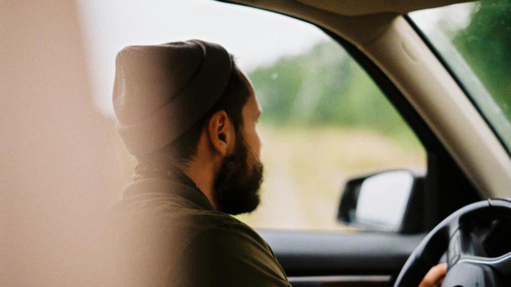 A man wearing a beanie driving a car and looking ahead.