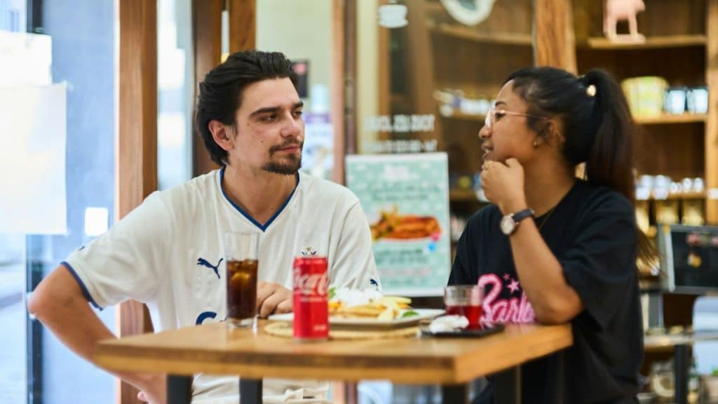 A bearded man with dark hair and a light shirt looks at a woman with dark hair.