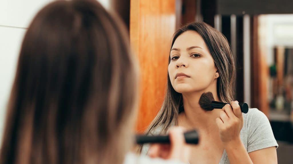 A woman applies makeup while looking in the mirror.