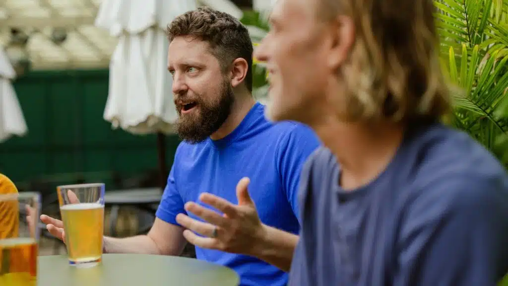 A man with a beard gestures with his hands while talking to a friend.