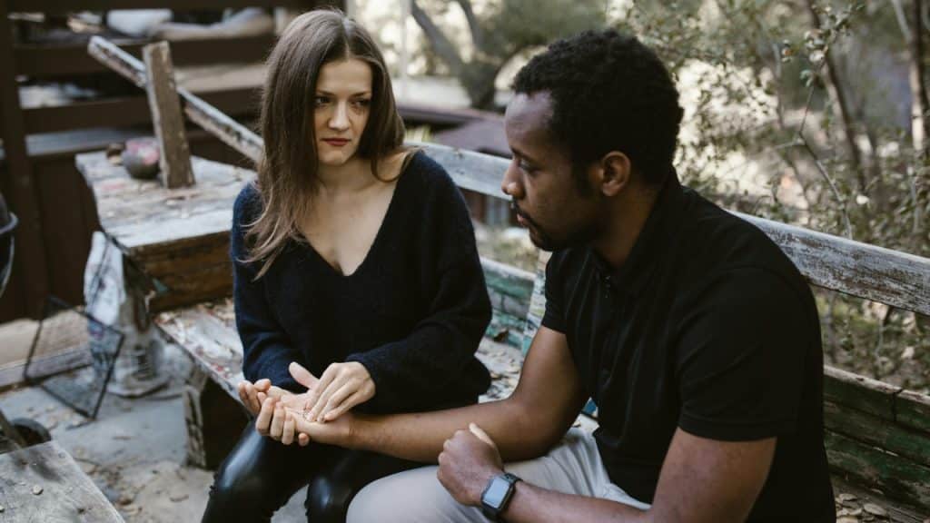 A woman gently holds a man's hand while they sit together on a bench.