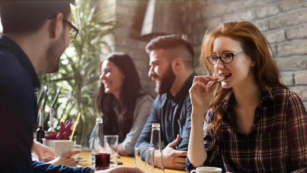 A woman in glasses eats a cracker at a table with three other people present.