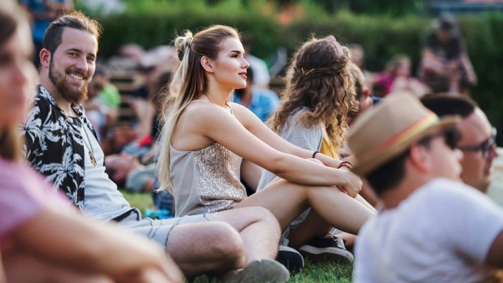 A group of young adults sit on the grass outdoors during an event.