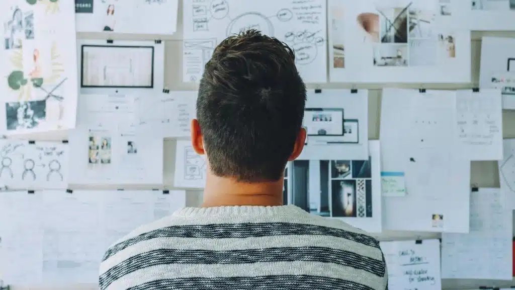 A man standing and looking at a wall covered with notes and design sketches.