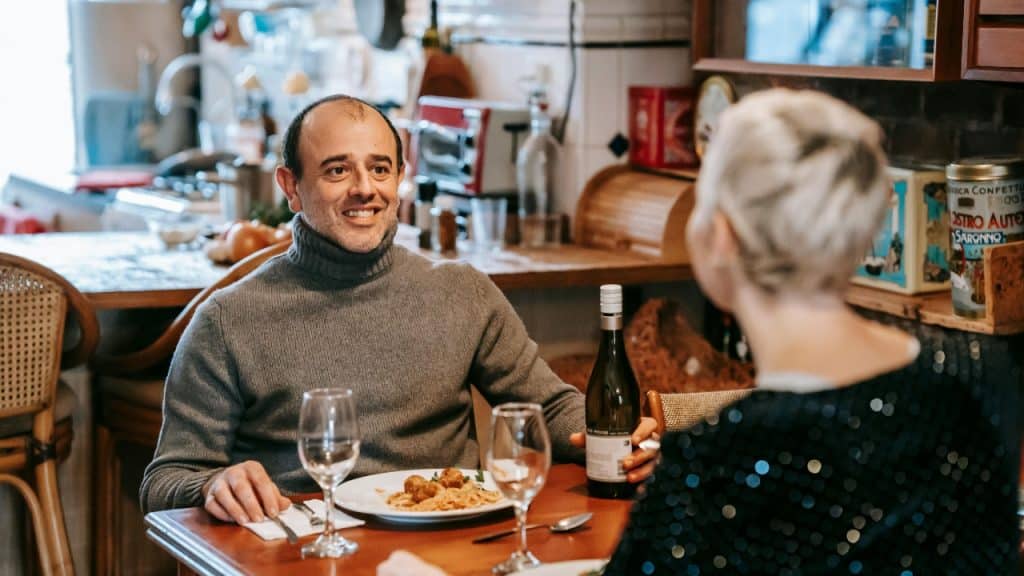 A man and a woman sit at a table in a kitchen having dinner together.