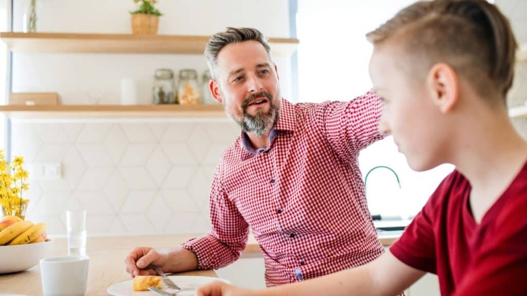A man in a plaid shirt speaks to a young person at a table.
