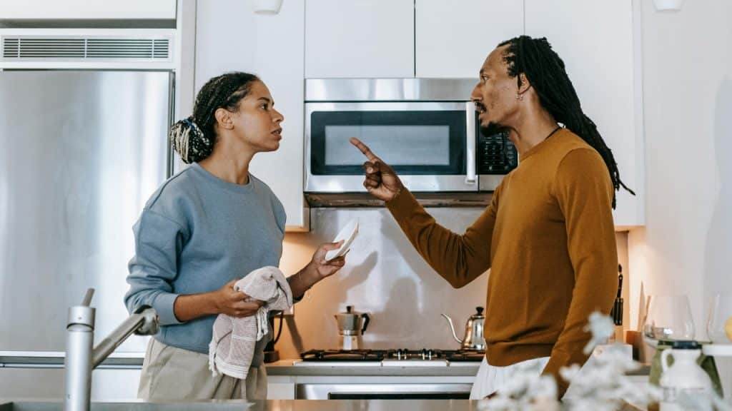 A man points his finger while arguing with a woman in a kitchen.