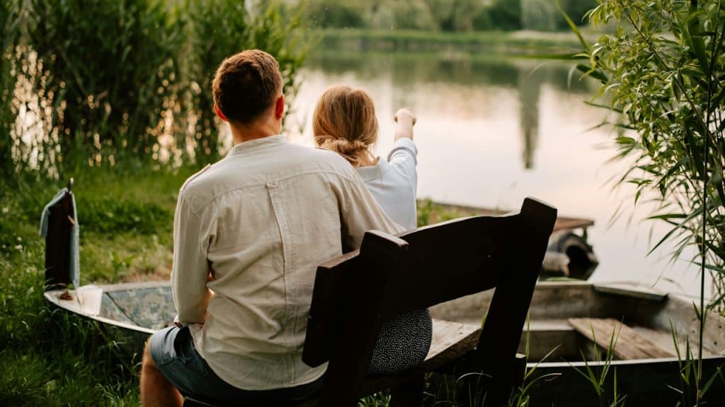 A man and a woman sitting on a bench by a lake.