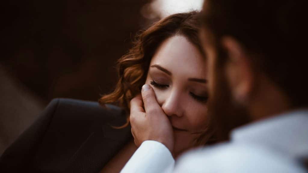 A hand gently cups a woman's face as she rests with her eyes closed.